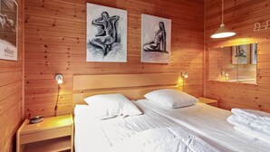 A wooden-paneled room with a bed, two paintings, a nightstand, and a mirror.