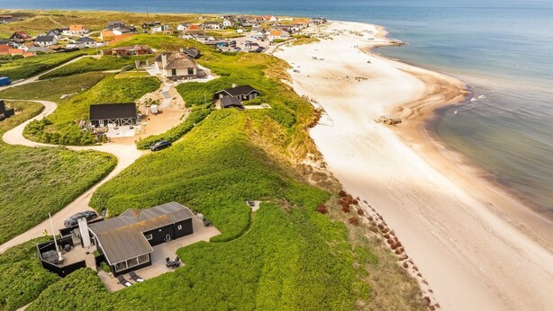 An aerial view of a coastal area with houses, a beach, and a large green field.