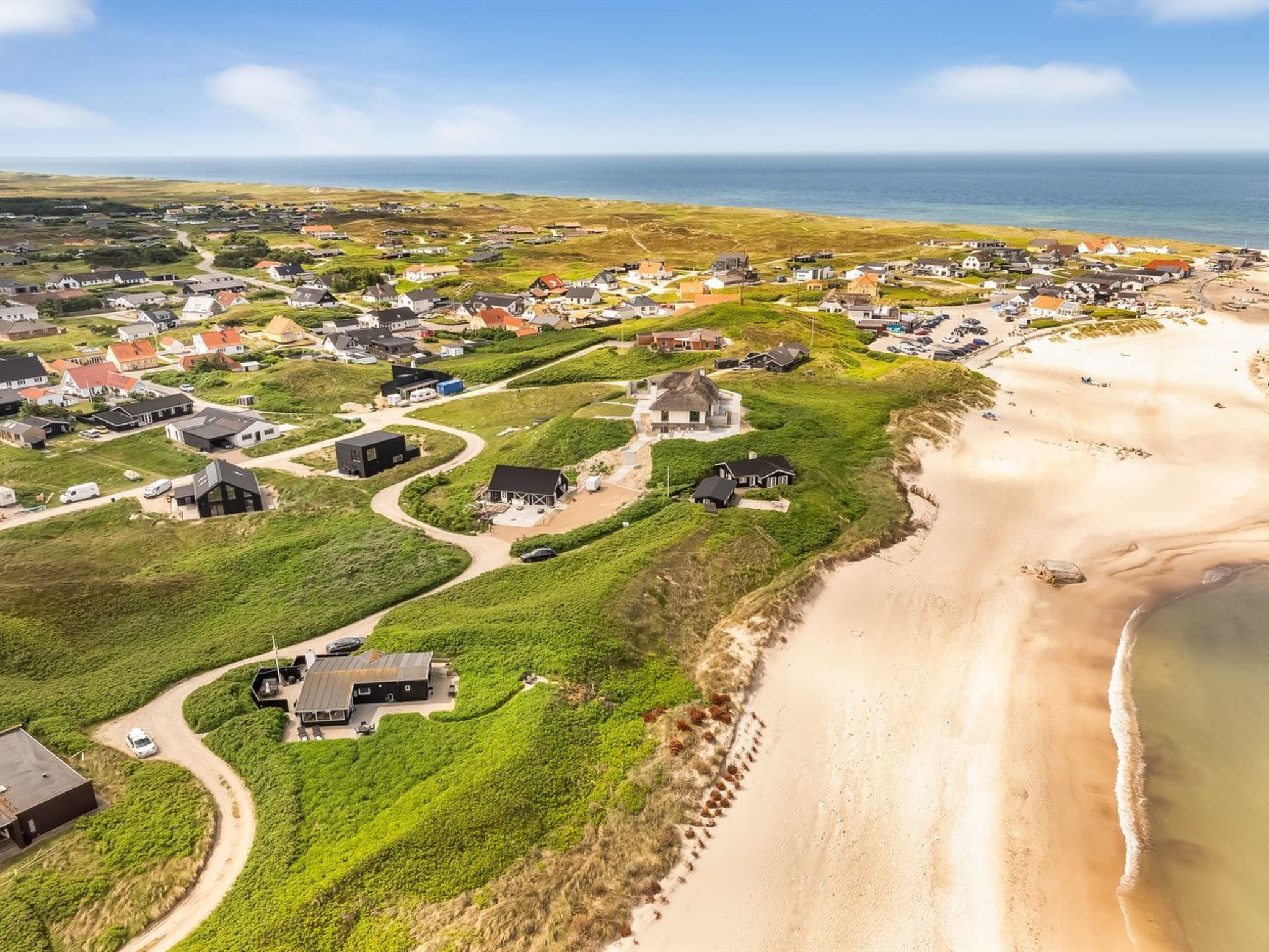 Vue aérienne d’une zone résidentielle côtière, avec des maisons, une plage et un ciel dégagé.