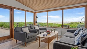 A spacious room with large windows, a wooden ceiling, and a view of greenery.