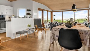 A modern kitchen with white cabinets, a dining area with a table and chairs, and a large window offering a view of the outdoors.