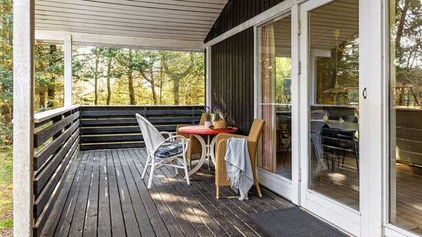 Une terrasse en bois avec une table et des chaises, une porte-fenêtre coulissante et une vue sur les arbres.