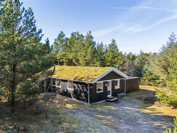 A cabin with a green roof, surrounded by trees.