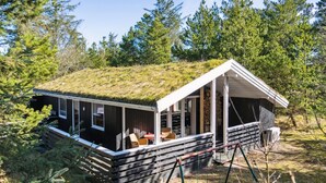 Une cabane avec un toit en herbe, une terrasse en bois et un porche couvert avec des sièges.