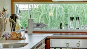 Une cuisine avec une fenêtre donnant sur un espace verdoyant, un évier et divers ustensiles de cuisine disposés sur le plan de travail.