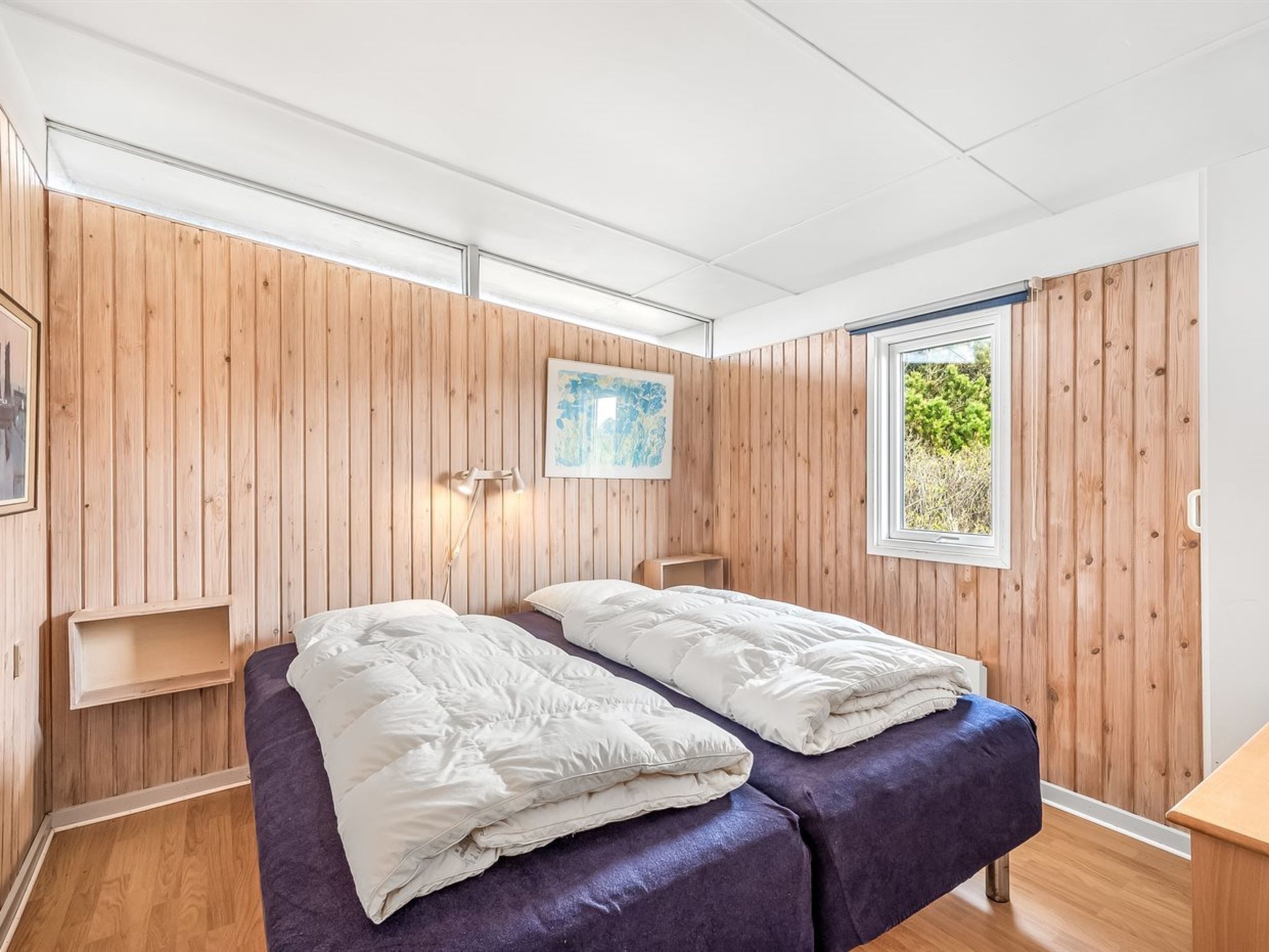 A bedroom with two beds, wooden walls, a window, and a painting.
