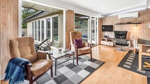 A modern living room with a glass door leading to a patio, a leather armchair, a small coffee table, and a television on a wooden wall.