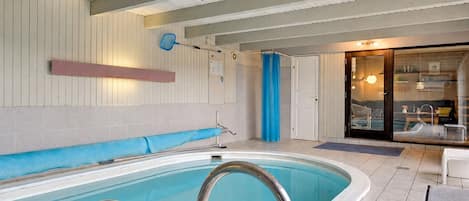 An indoor swimming pool with a clear view of the water, a blue towel rack, and a door leading to a room with a bed and a window.