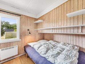 Een slaapkamer met een bed, een raam en houten lambrisering.