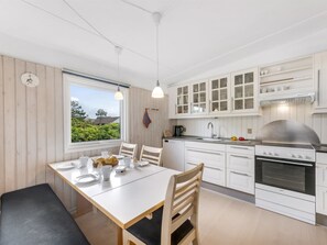 Una cocina moderna con armarios blancos, una mesa de comedor para cuatro personas y un ventanal con vistas a zonas verdes.
