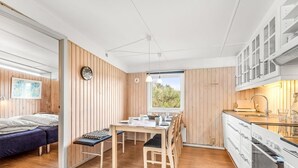 A compact kitchen with wooden walls, a dining area with a table and chairs, and a bed in the adjacent room.
