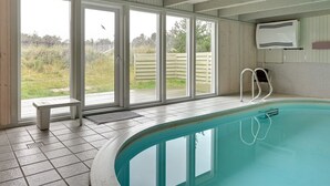 A swimming pool with a view of a garden through large sliding glass doors.