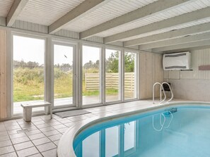 Une piscine intérieure avec vue sur l’extérieur, un banc et une échelle.