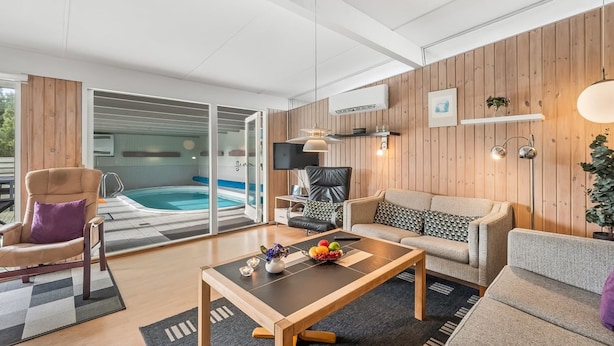 A modern living room with a pool, wooden walls, a sofa, a coffee table, and a TV.
