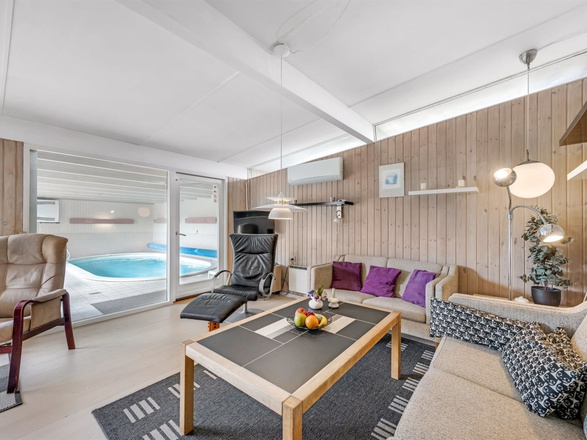 A modern living room with a pool, a sofa, a chair, and a coffee table with fruit.