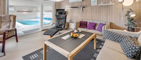 A modern living room with a pool, a sofa, a chair, and a coffee table with fruit.