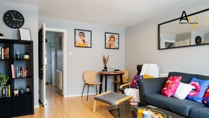 A modern living room with a sofa, coffee table, and bookshelf. There is a dining area with chairs and a table. - Flexible 2-Bed House: Ideal for Business Trips (Northampton)