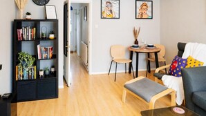 A modern living room with a bookshelf, a grey sofa, a small round table, and a wooden bench. - Flexible 2-Bed House: Ideal for Business Trips (Northampton)