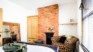 A cozy room with a brick fireplace, a leopard-print armchair, and a bed with a green blanket.
