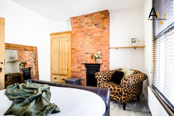 Una habitación acogedora con una chimenea de ladrillo, un sillón estampado de leopardo y una cama con manta verde.