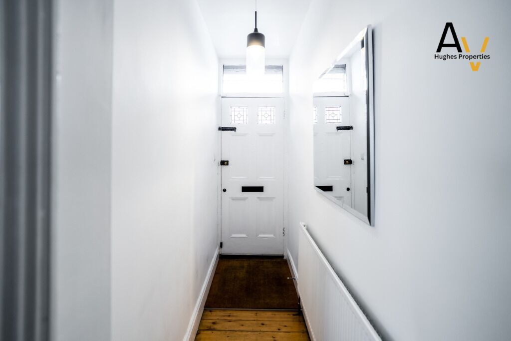 A narrow hallway with white walls, a wooden floor, and a ceiling light.
