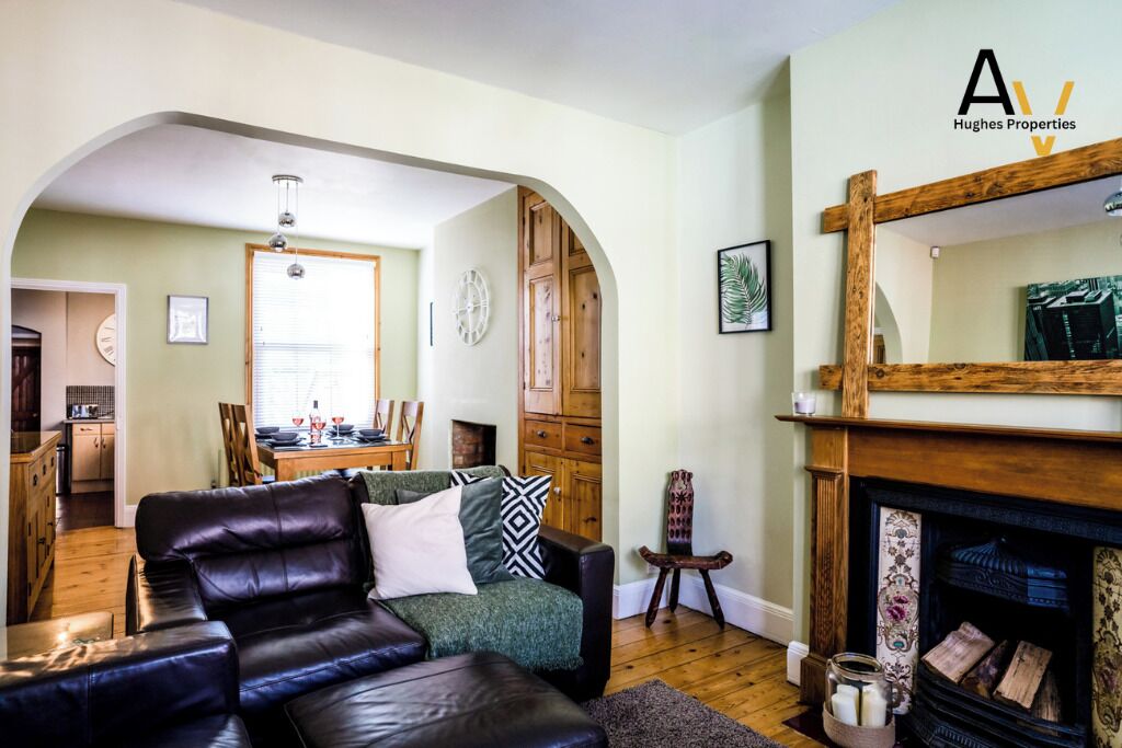 Ein Wohnzimmer mit Kamin, ein Essbereich mit Tisch und Stühlen sowie eine Küche im Hintergrund.