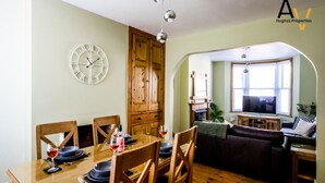 A dining area with a wooden table, chairs, and a wall-mounted clock.