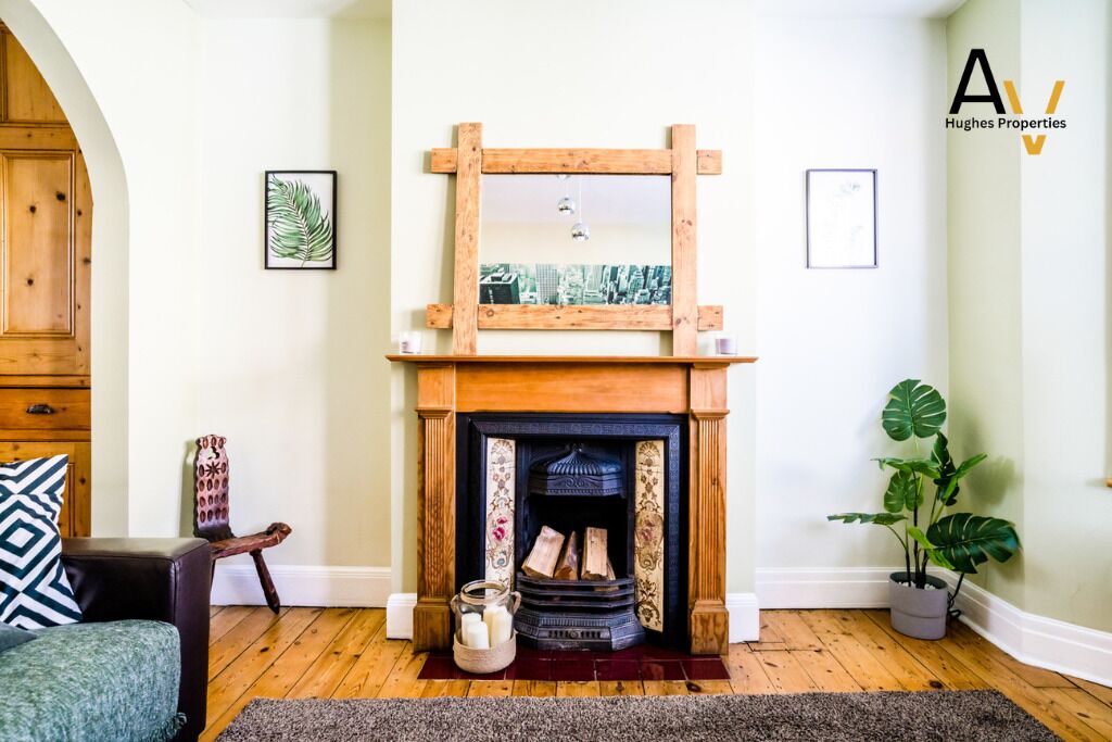 A cozy living room with a fireplace, a wooden mantel, a framed mirror, and a potted plant.