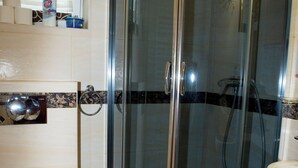 A bathroom with a glass-enclosed shower, a toilet, a sink, and a window with blinds.