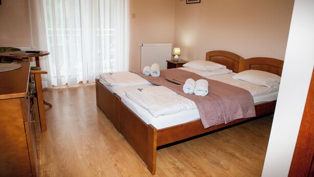 A hotel room with a wooden bed, a desk with a chair, a lamp, and a window with sheer curtains.
