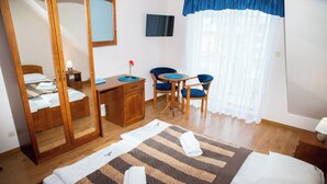 A hotel room with a bed, a desk, a chair, a TV, and a mirror.