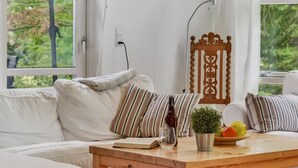 Une pièce chaleureuse avec un canapé blanc, des coussins à rayures, une table d’appoint en bois sur laquelle se trouvent un livre, un verre et une bouteille.