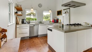 Une cuisine moderne avec des meubles blancs, un îlot central, des appareils en acier inoxydable et des luminaires suspendus.