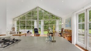Une cuisine spacieuse avec un grand îlot central, un coin repas avec une table et des chaises, et une vue sur le jardin grâce à de grandes fenêtres.