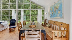 Un coin repas avec une grande table, des chaises et un banc. Il y a une carte accrochée au mur et une bouteille de vin sur la table.