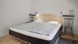 A bedroom with a wooden headboard, a bed with a floral bedspread, two bedside tables with lamps, and a green chair.