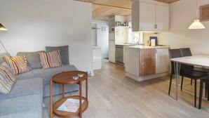 A modern kitchen with wooden cabinets, a dining area with a table and chairs, and a living area with a sofa and a small round table.
