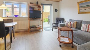 A living room with a wooden ceiling, a television on a wooden stand, a sofa, a chair, a small table, and a window with a view of the outside.