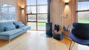 Een modern interieur met een houten vloer, een blauwe bank, een zwarte stoel, een open haard en een groot raam.