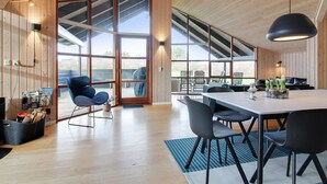 Een ruime kamer met een grote eettafel, meerdere stoelen en een hoog plafond met houten balken.