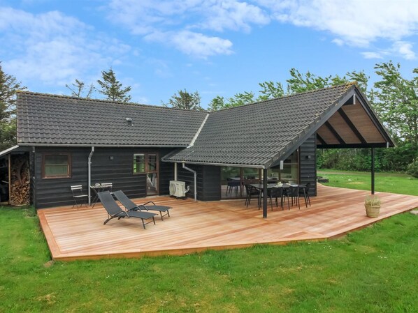 A modern log cabin with a deck, outdoor seating, and a covered patio area.