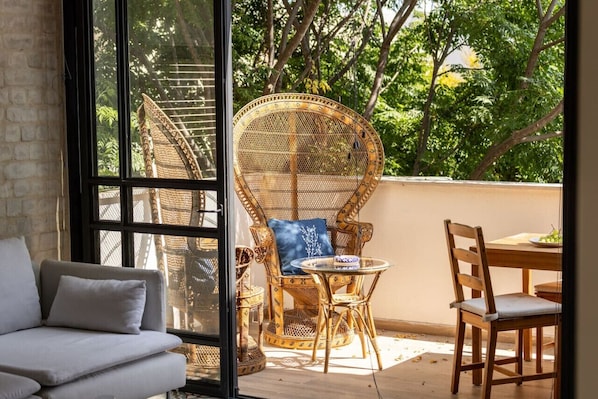A room with a sofa, wicker chairs, a dining table, and a large window overlooking greenery.