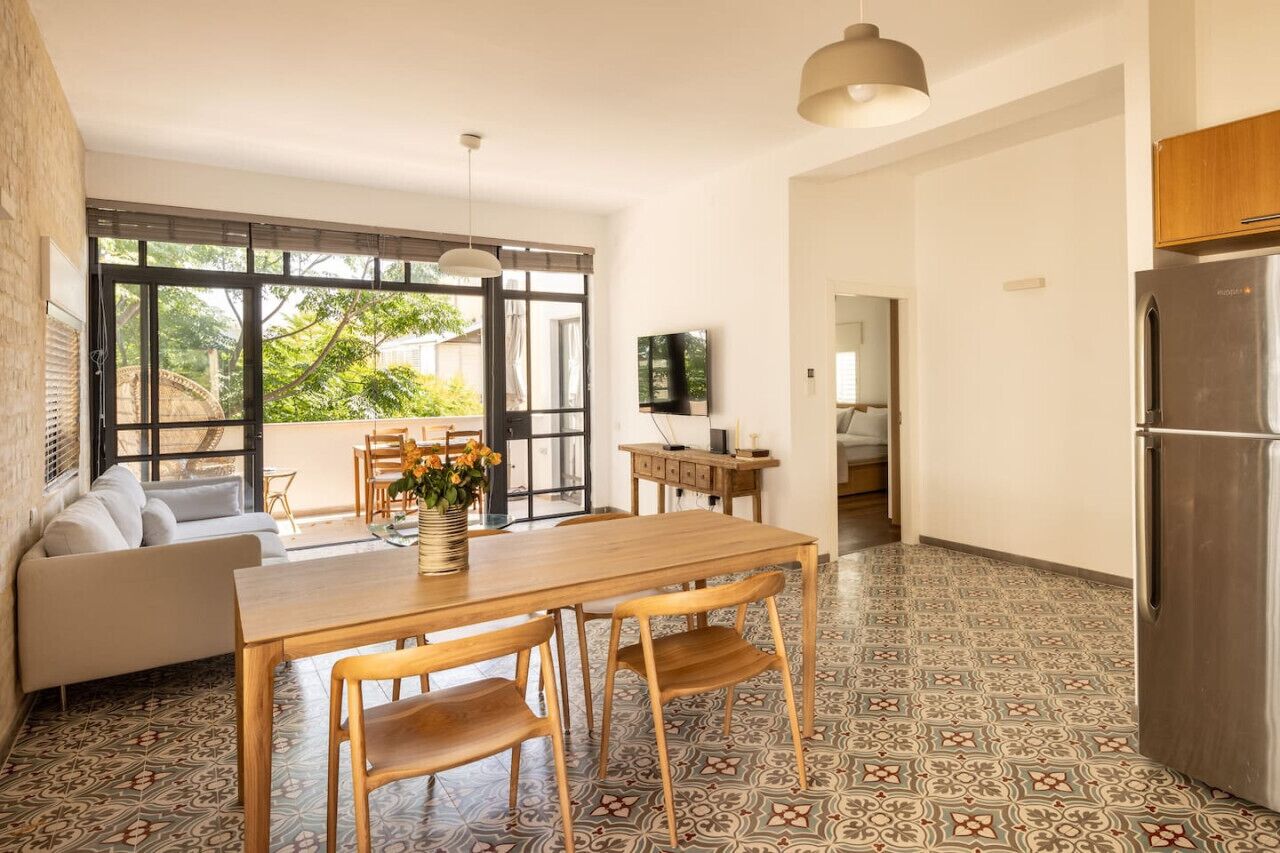 A modern kitchen with a dining area, large windows, and a refrigerator.