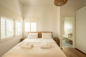 A bedroom with a large bed, two bedside tables, a wooden headboard, and a view of the bathroom. - Rustic Charm Tel Aviv CTR by Sea N' Rent (Tel Aviv)