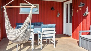 Un espace extérieur aménagé avec une zone salon couverte, comprenant un hamac, des chaises blanches et un canapé bleu.