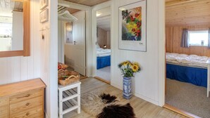 Une chambre confortable aux murs en bois, avec un lit recouvert d’une literie bleue, une petite commode blanche, une table de chevet en bois, un tableau encadré et un vase rempli de tournesols.