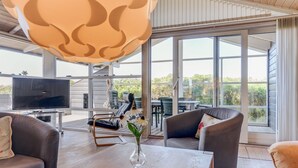 Uma sala de estar moderna com televisão, assentos confortáveis, uma mesa de centro e uma janela grande com vista para o verde.