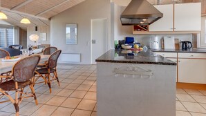 Uma cozinha moderna com ilha central, vigas de madeira no teto e área de refeições com cadeiras de vime.