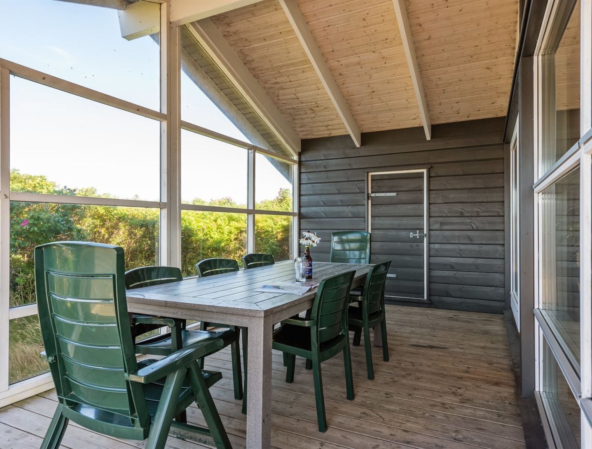 A covered outdoor area with a table and chairs, large windows, and a door.