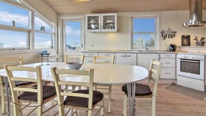 Una cocina moderna con armarios blancos, una mesa de comedor redonda y un ventanal con vistas al cielo.
